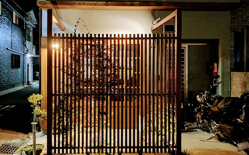 ライトアップされた植栽、格子から漏れる灯り、京町家らしい風情が感じられる夜の外観。